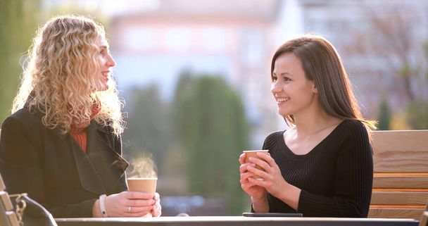 Щасливі молоді жінки друзі п'ють каву в міському ресторані на вулиці під час робочої перерви. Концепція спілкування та дружби
. - Фото, зображення