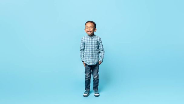 Happy childhood. Full length portrait of adorable little african american boy smiling to camera, posing over blue studio background, panorama with free space - Photo, image