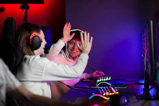 νεαροί παίκτες με ακουστικά παίζουν ένα παιχνίδι στον υπολογιστή και συναισθηματικά χαίρονται με τη νίκη σε ένα κλαμπ υπολογιστών τη νύχτα - Φωτογραφία, εικόνα