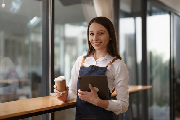 Νεαρή γυναίκα διευθυντής στο εστιατόριο με tablet. Γυναίκα ιδιοκτήτης καφετέριας με ανοιχτή πινακίδα. Έννοια των μικρών επιχειρήσεων. - Φωτογραφία, εικόνα
