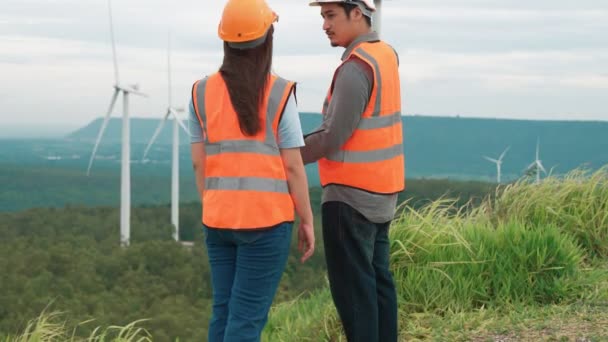 田舎の丘や山の上の風力発電所で働く男性と女性のエンジニア。再生可能エネルギー、持続可能なエネルギーの将来の生産のための進歩的な理想. - 映像、動画