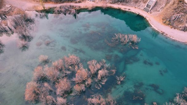 Turkuaz mavi ayna suyu ve gölde ağaçlar. Su altı akıntılarından gelen ışık çizgileri görülebilir. Sonbahar dağları ve kozalaklı ağaçlar suya yansıyor. Issyk Dağı Gölü, Kazakistan - Fotoğraf, Görsel
