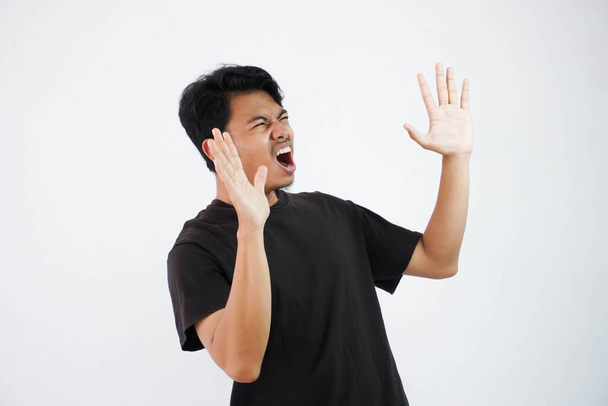huutanut tai järkyttynyt nuori aasialainen mies avoin käsi suu auki yllään musta t paita eristetty valkoisella pohjalla - Valokuva, kuva