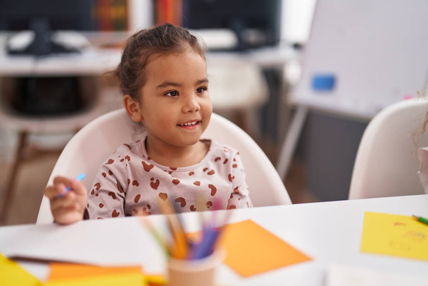Симпатичная латиноамериканка, сидящая за столом и рисующая на бумаге в детском саду. - Фото, изображение
