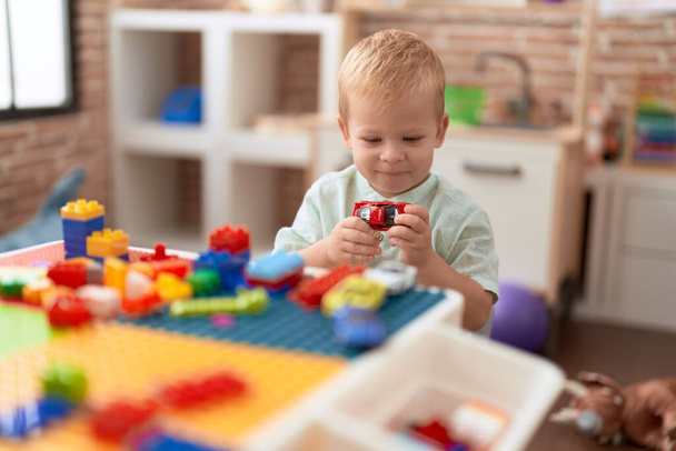 Liebenswertes Kleinkind, das im Kindergarten mit Auto und Spielzeug und Bauklötzen spielt - Foto, Bild
