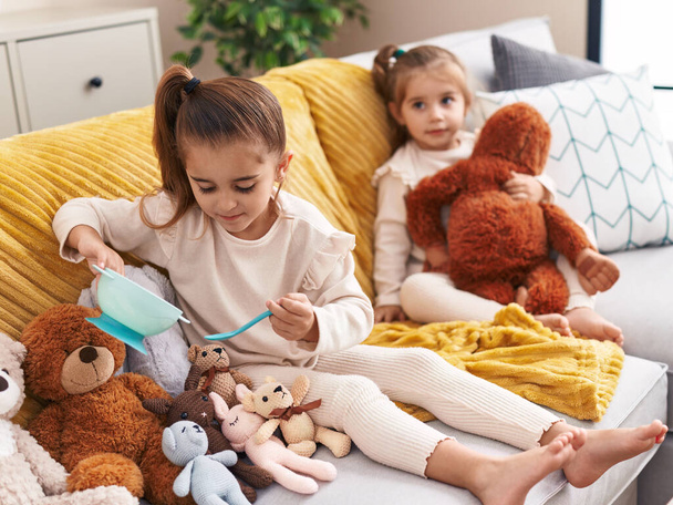 Due bambini che giocano con le bambole seduti sul divano di casa - Foto, immagini