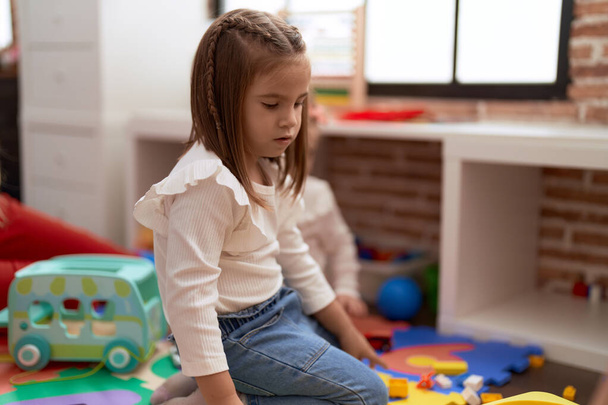Adorable hispanic girl sitting on floor with relaxed expression at kindergarten - Foto, Bild