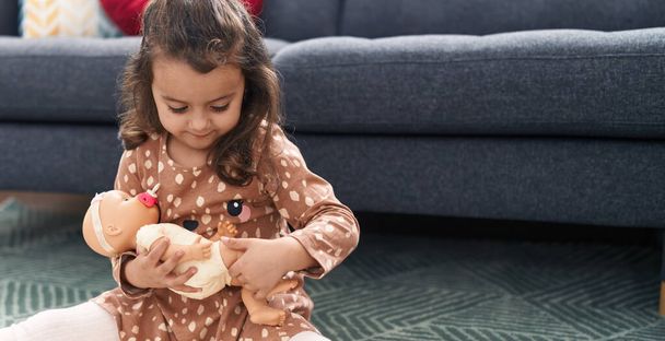 Urocza latynoska dziewczyna przytula lalkę siedząc na podłodze w domu - Zdjęcie, obraz