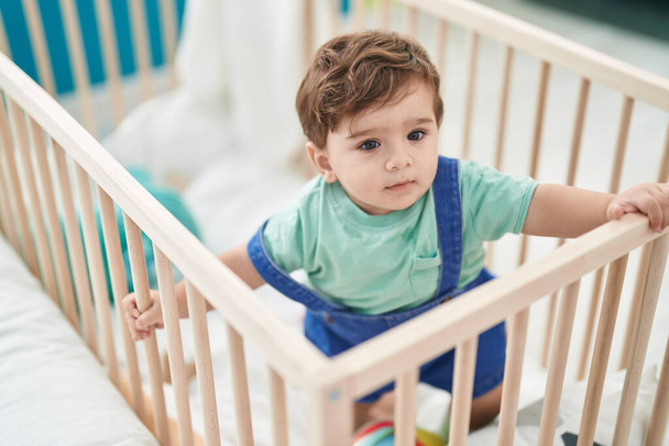 Liebenswertes hispanisches Kleinkind steht auf Wiege im Schlafzimmer - Foto, Bild