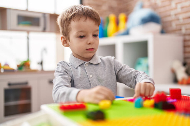 Adorable toddler playing with construction blocks sitting on table at kindergarten - Foto, imagen