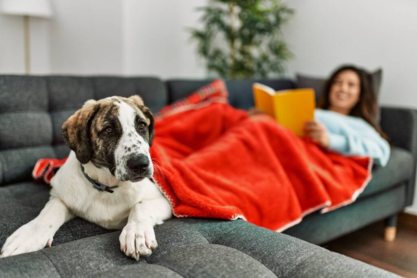 Jovem mulher lendo livro deitado no sofá com cão em casa - Foto, Imagem