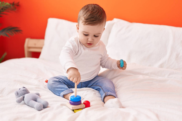 Adorable bebé caucásico jugando con juguetes sentados en la cama en el dormitorio - Foto, Imagen