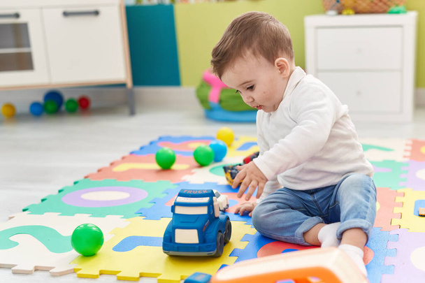 Adorable caucasian baby playing with truck toy sitting on floor at kindergarten - 写真・画像