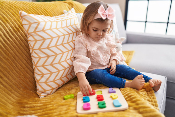 Adorable blonde toddler playing with maths puzzle game sitting on sofa at home - Photo, Image
