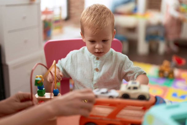 Liebenswertes Kleinkind spielt mit Autospielzeug auf Tisch im Kindergarten - Foto, Bild