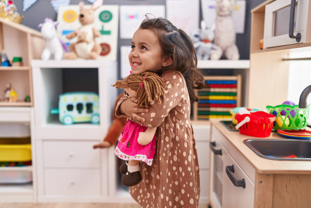 Adorable hispanic girl hugging doll standing at kindergarten - Valokuva, kuva