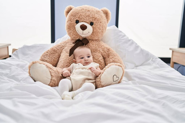 Adorable bebé relajado acostado en la cama con oso de peluche en el dormitorio - Foto, Imagen