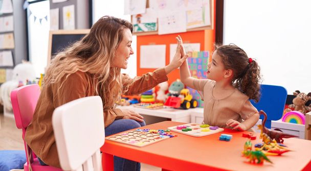 Adorável menina hispânica jogando com matemática jogo de puzzle alta cinco com o professor no jardim de infância - Foto, Imagem