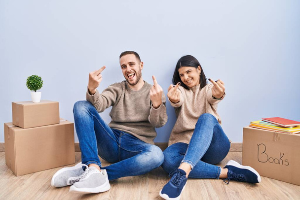 Young couple moving to a new home showing middle finger doing fuck you bad expression, provocation and rude attitude. screaming excited  - Foto, Imagen