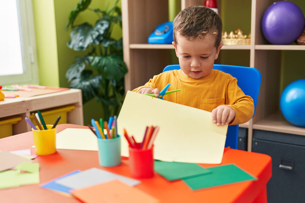 Adorable garçon caucasien coupant du papier assis sur la table à la maternelle - Photo, image