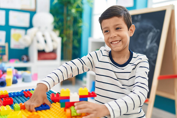幼稚園でテーブルの上に座っている建設ブロックと遊んで愛らしいヒスパニック系の男の子 - 写真・画像