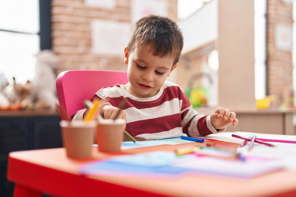 幼稚園のテーブルに座ってノートに描く愛らしい幼児の学生 - 写真・画像