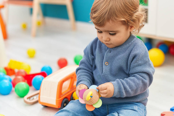 Uroczy latynoski maluch trzymający zabawkę na podłodze w przedszkolu - Zdjęcie, obraz