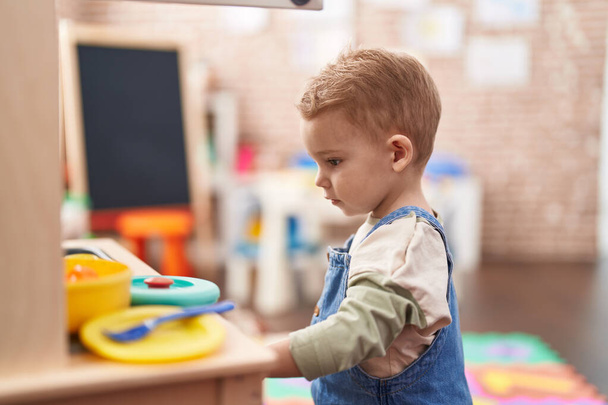 Adorable toddler playing with play kitchen standing at kindergarten - Foto, imagen