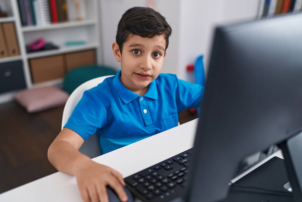Liebenswert hispanischer Junge Student mit Computer sitzt auf Tisch im Klassenzimmer - Foto, Bild