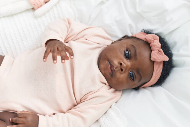 Bébé afro-américain couché sur le lit avec une expression détendue dans la chambre - Photo, image