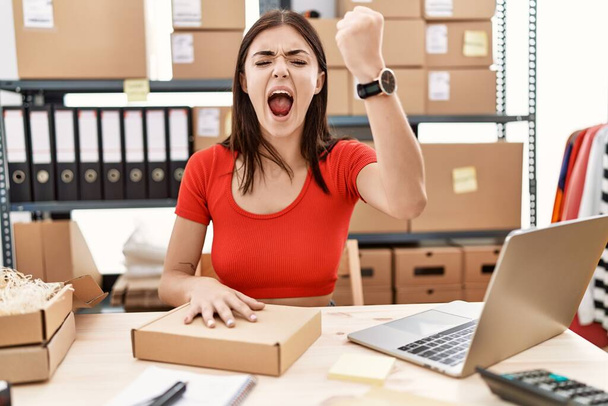 Young hispanic woman preparing order working at storehouse angry and mad raising fist frustrated and furious while shouting with anger. rage and aggressive concept.  - Photo, Image