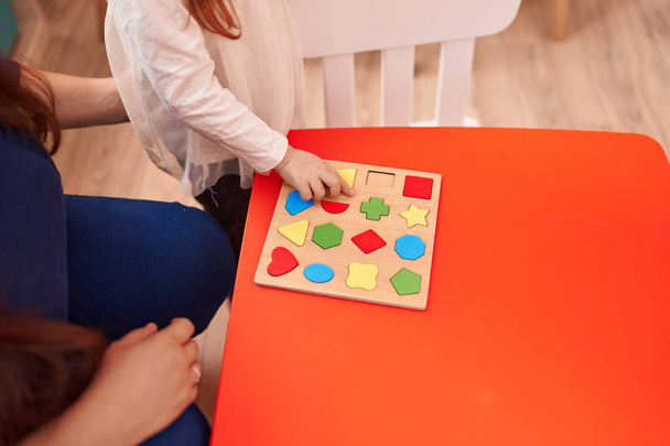 Menina ruiva adorável jogando com jogo de quebra-cabeça geometria sentado na mesa no jardim de infância - Foto, Imagem