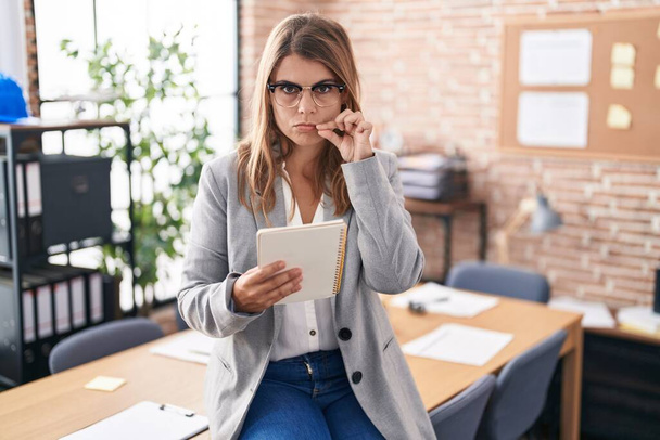 Jeune femme hispanique travaillant au bureau portant des lunettes bouche et lèvres fermées comme zip avec les doigts. secret et silencieux, tabou parlant  - Photo, image