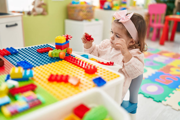Adorable blonde toddler playing with construction blocks sitting on table at kindergarten - Foto, Imagen