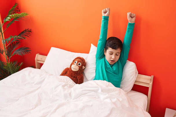 Schattige Spaanse jongen die zijn armen uitstrekt in de slaapkamer. - Foto, afbeelding
