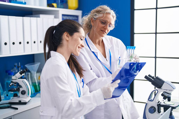 Deux femmes scientifiques écrivent sur un document contenant des éprouvettes en laboratoire - Photo, image