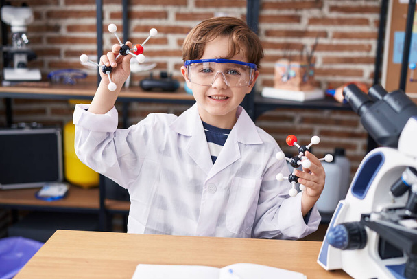 Entzückender hispanischer Student lächelt selbstbewusst und hält Moleküle im Labor-Klassenzimmer - Foto, Bild