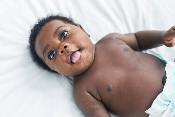 Bambino afroamericano sorridente fiducioso sdraiato sul letto in camera da letto - Foto, immagini