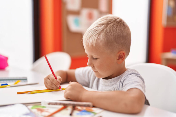Not defterine resim çizen sevimli çocuk sınıftaki masada oturuyor. - Fotoğraf, Görsel