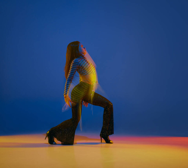 Talented. Portrait of young girl dancing heels dance over blue background in neon with mixed lights. Concept of dance lifestyle, modern style, contemporary dance, youth culture, self-expression - Fotó, kép