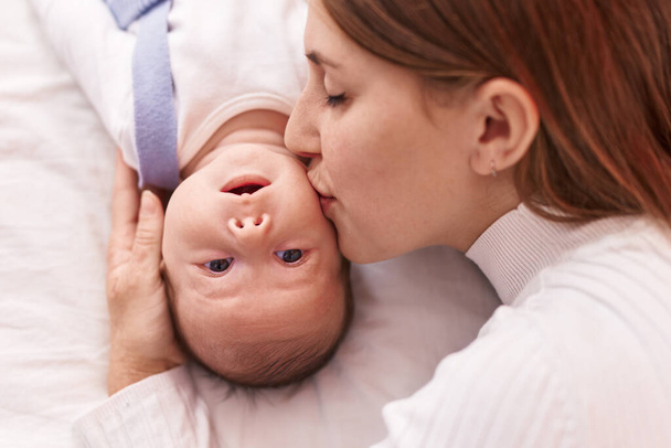 Anne ve oğlu yatakta uzanıp bebeği öpüyor. - Fotoğraf, Görsel