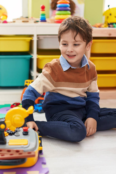 Adorable hispanic boy playing with technician tools toy sitting on floor at kindergarten - Foto, Bild