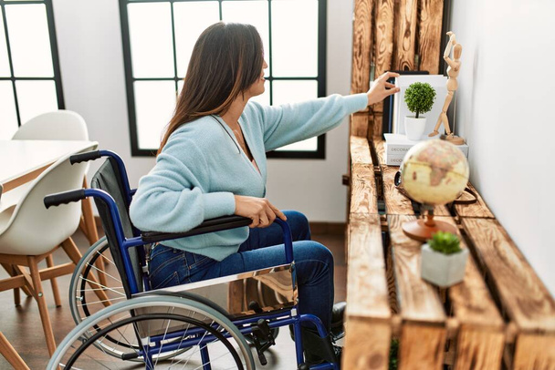 Młoda kobieta trzyma książkę na wózku inwalidzkim pracując w domu - Zdjęcie, obraz