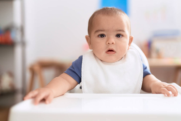 Adorable chinese toddler wearing bib sitting on dinner chair baby at home - Photo, Image
