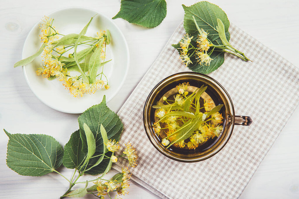 Плоский вид на Tilia platyphyllos известный как крупнолистная липа цветущий травяной чай из свежесобранных цветов с листьями деревьев и ветвей с цветами для украшения на домашнем столе. - Фото, изображение