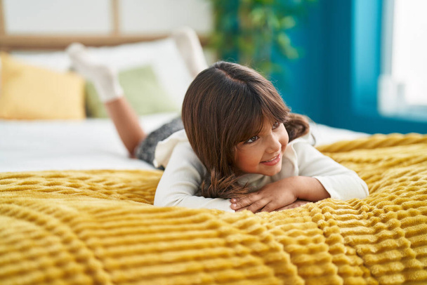 Adorable fille hispanique souriant confiant couché sur le lit dans la chambre - Photo, image