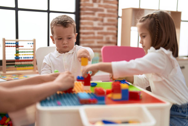 Очаровательная девочка и мальчик играют со строительными блоками, сидя на столе в детском саду - Фото, изображение