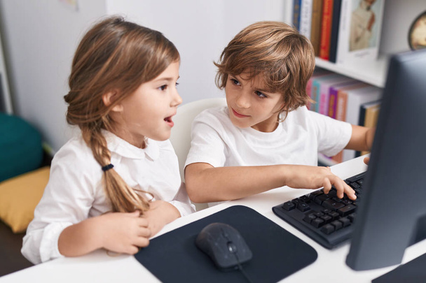 Брат і сестра студенти використовують комп'ютер, сидячи на столі в класі - Фото, зображення