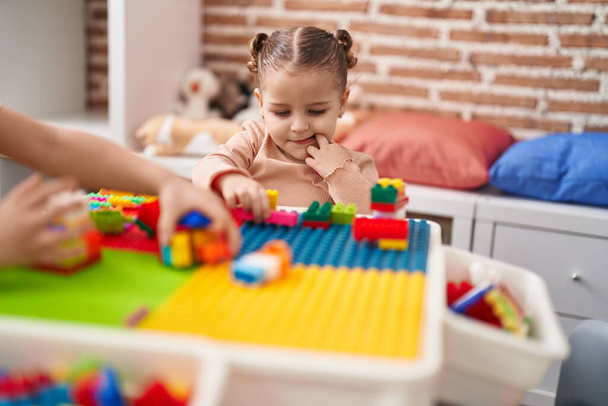 Adorable chica hispana jugando con bloques de construcción sentada en la mesa en el jardín de infantes - Foto, imagen
