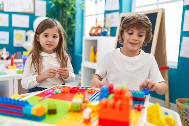 Hermano y hermana jugando con bloques de construcción sentados en la mesa en el jardín de infantes - Foto, Imagen